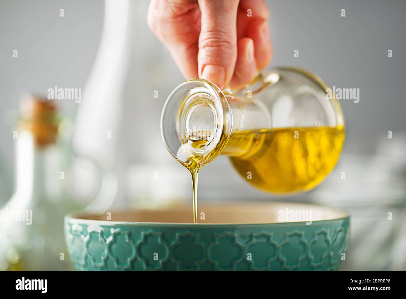 Bottle of virgin olive oil pouring to bowl close up Stock Photo