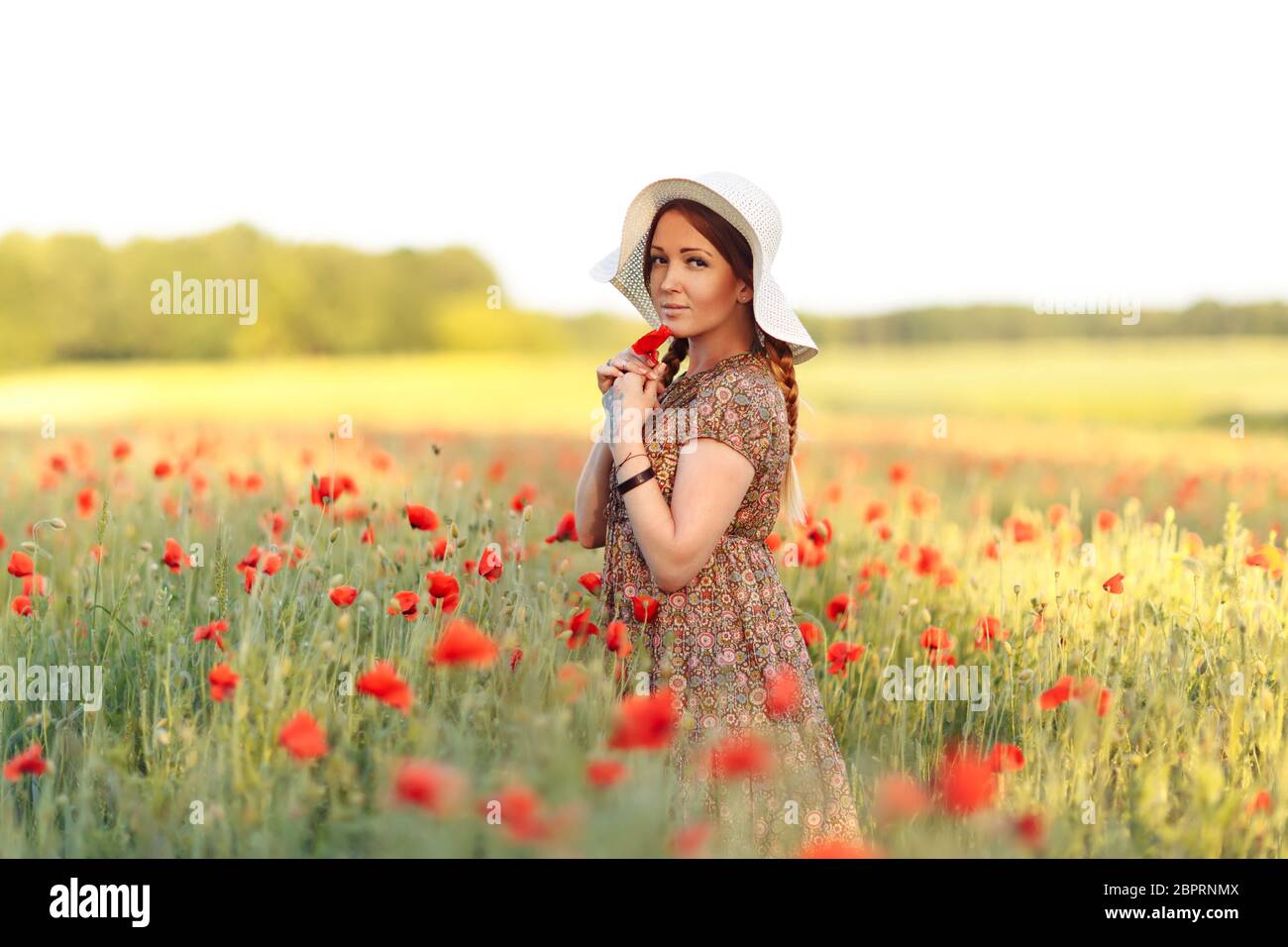 Beautiful redhead woman in white hat posing on green field with poppies ...
