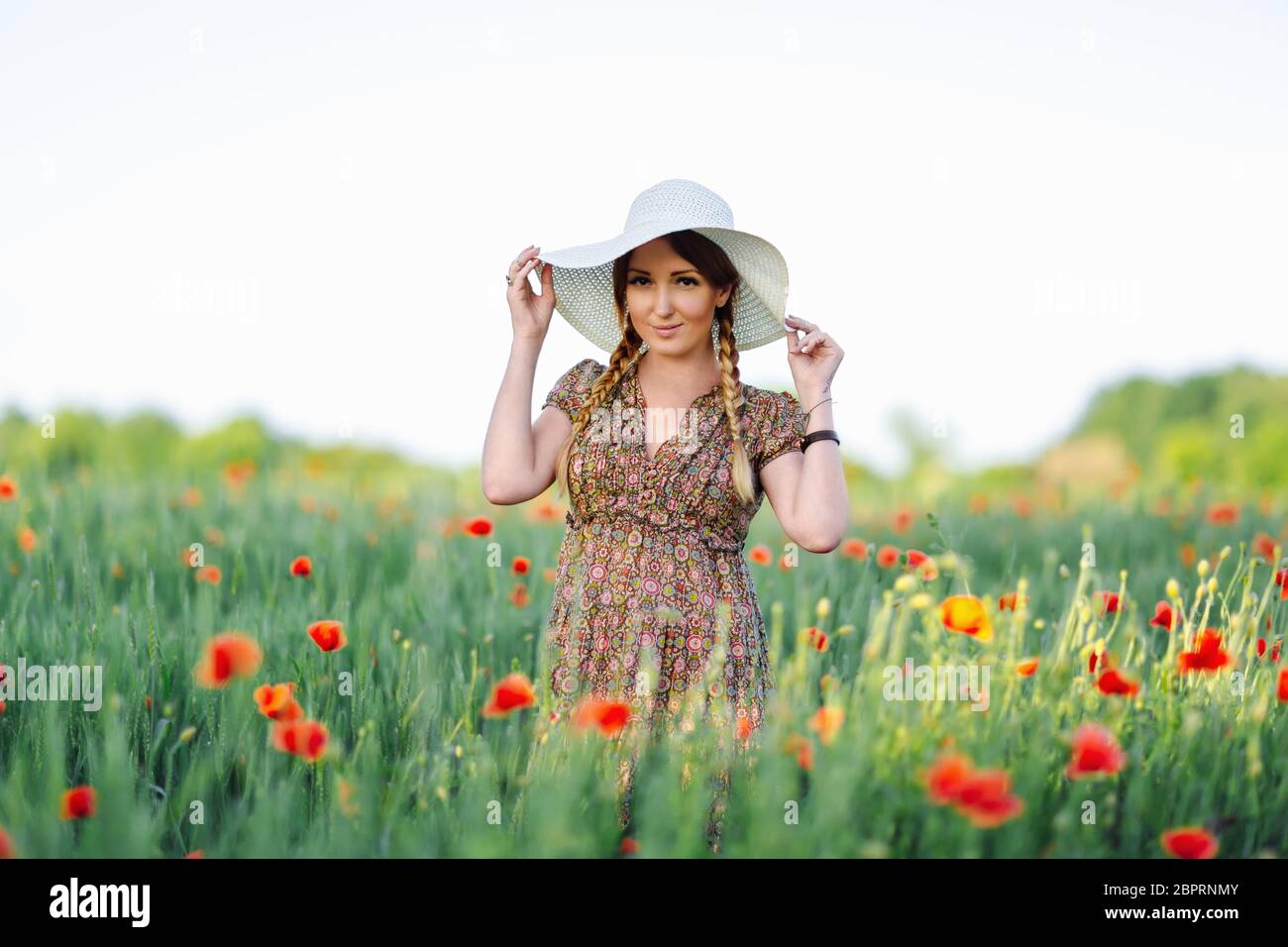 Beautiful redhead woman in white hat posing on green field with poppies ...