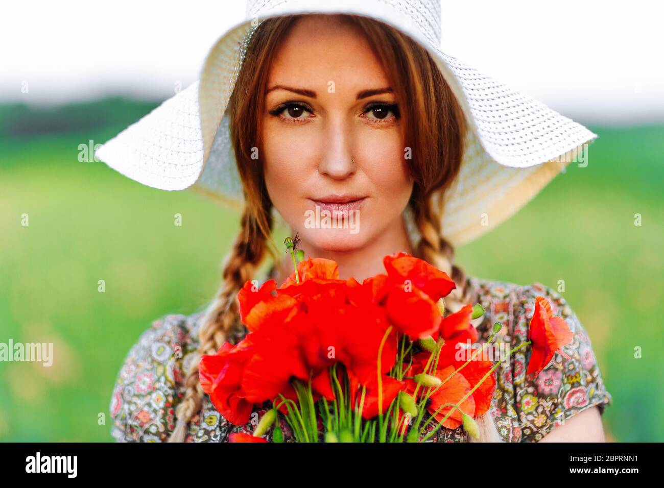 Portrait of beautiful redhead woman in hat on green field with bouquet ...