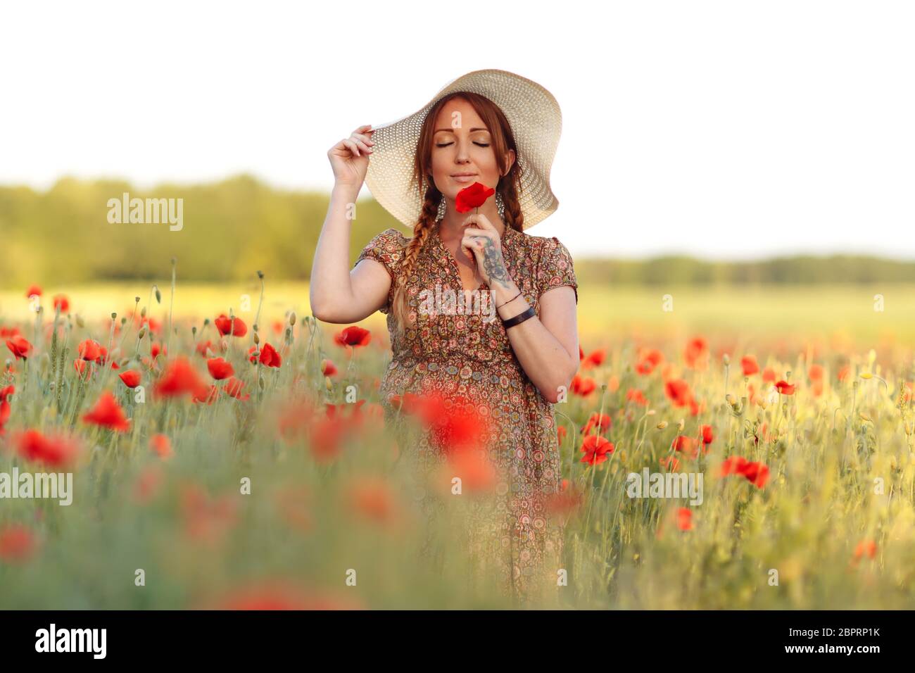 Beautiful redhead woman in white hat posing on green field with poppies ...