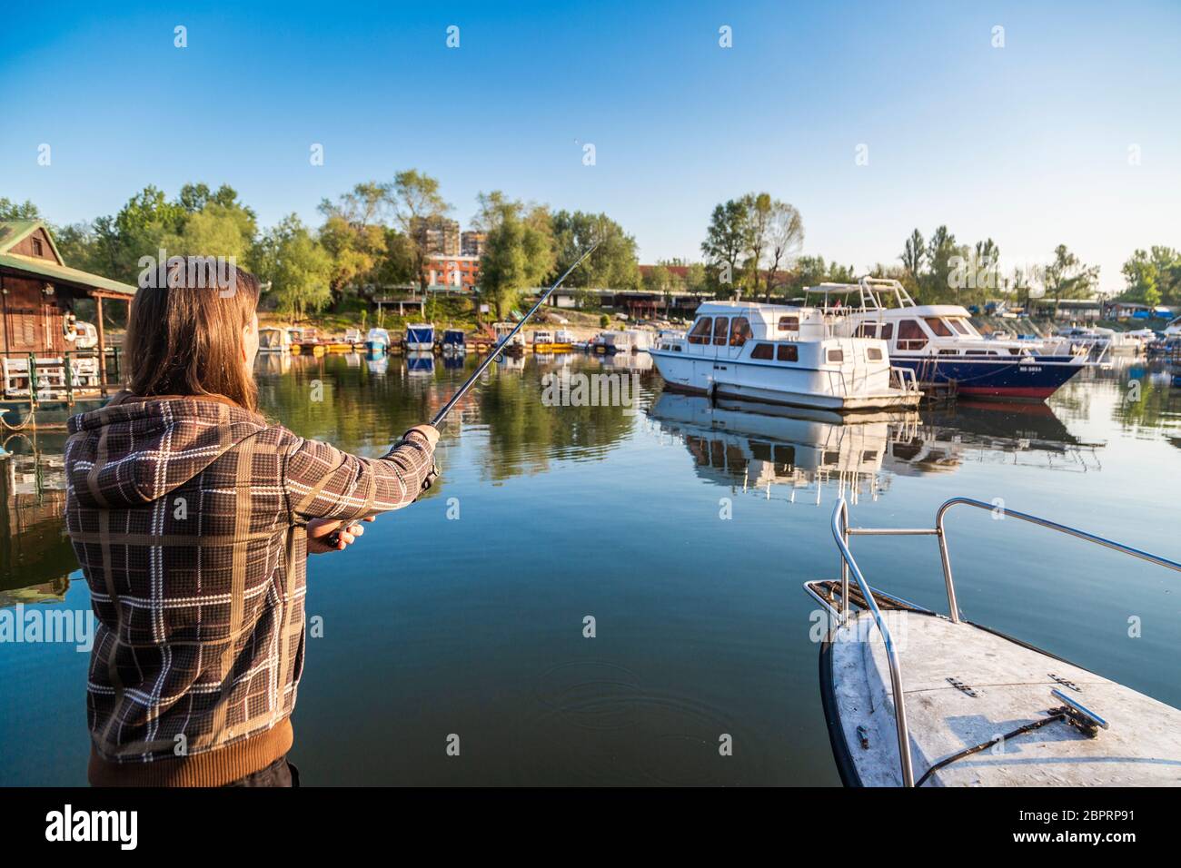 https://c8.alamy.com/comp/2BPRP91/man-with-long-hair-is-fishing-at-river-corner-from-raft-boats-and-floating-houses-are-around-him-with-trees-in-background-he-is-using-fishing-rod-wi-2BPRP91.jpg