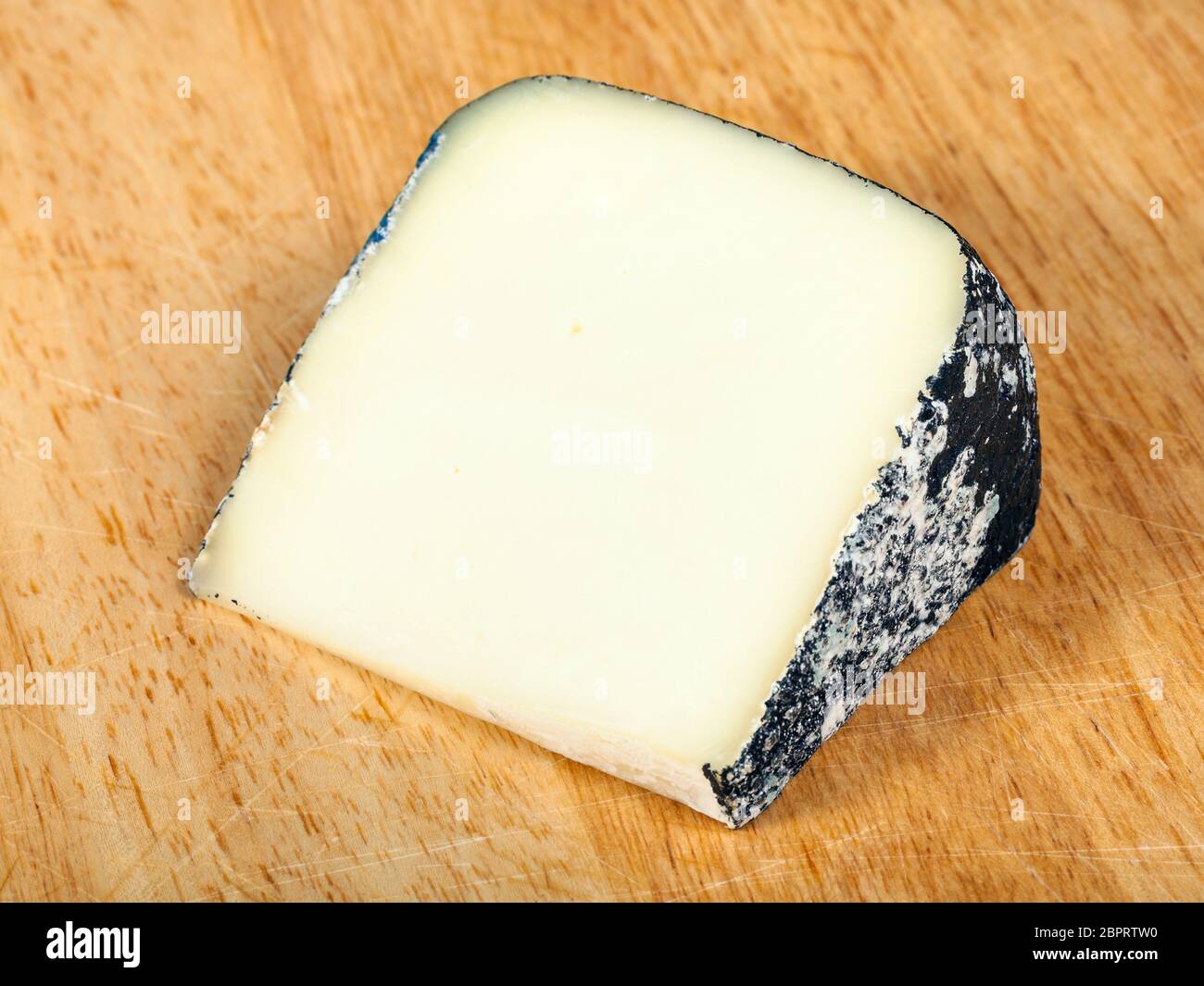 piece of local italian Perla Nera sheep's milk cheese on light wooden cutting board Stock Photo