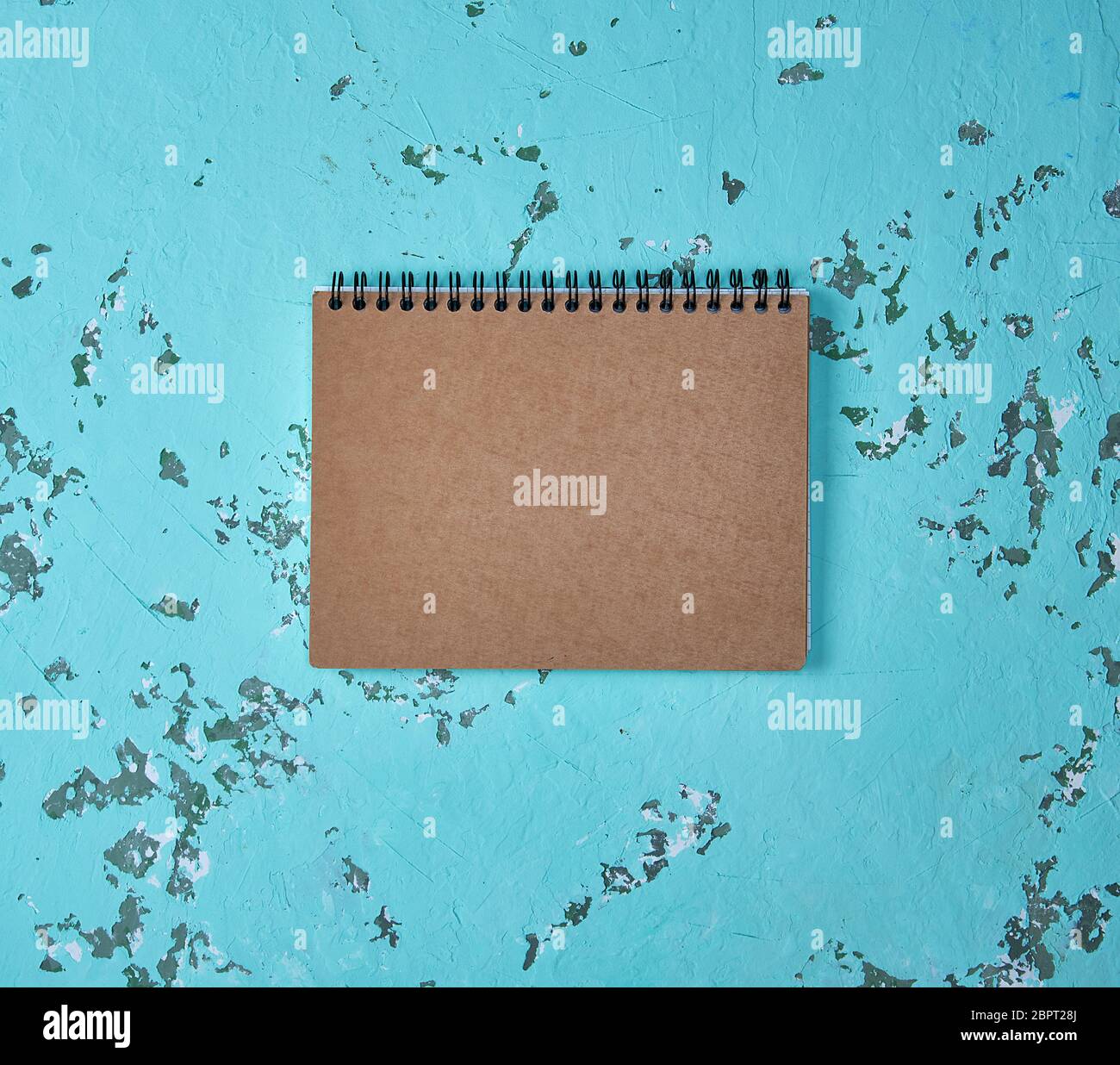 empty notebook on a black iron spring with brown empty sheets on a green background, close up Stock Photo