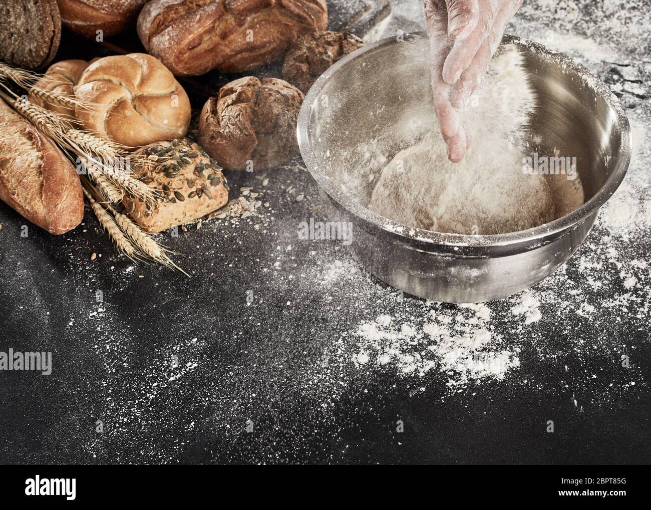 Baker dusting his dough with flour from his hands as he prepares the