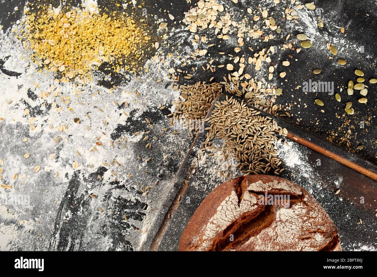 Assorted grain seeds with a freshly baked crusty loaf of bread and flour on a messy kitchen counter viewed from above Stock Photo
