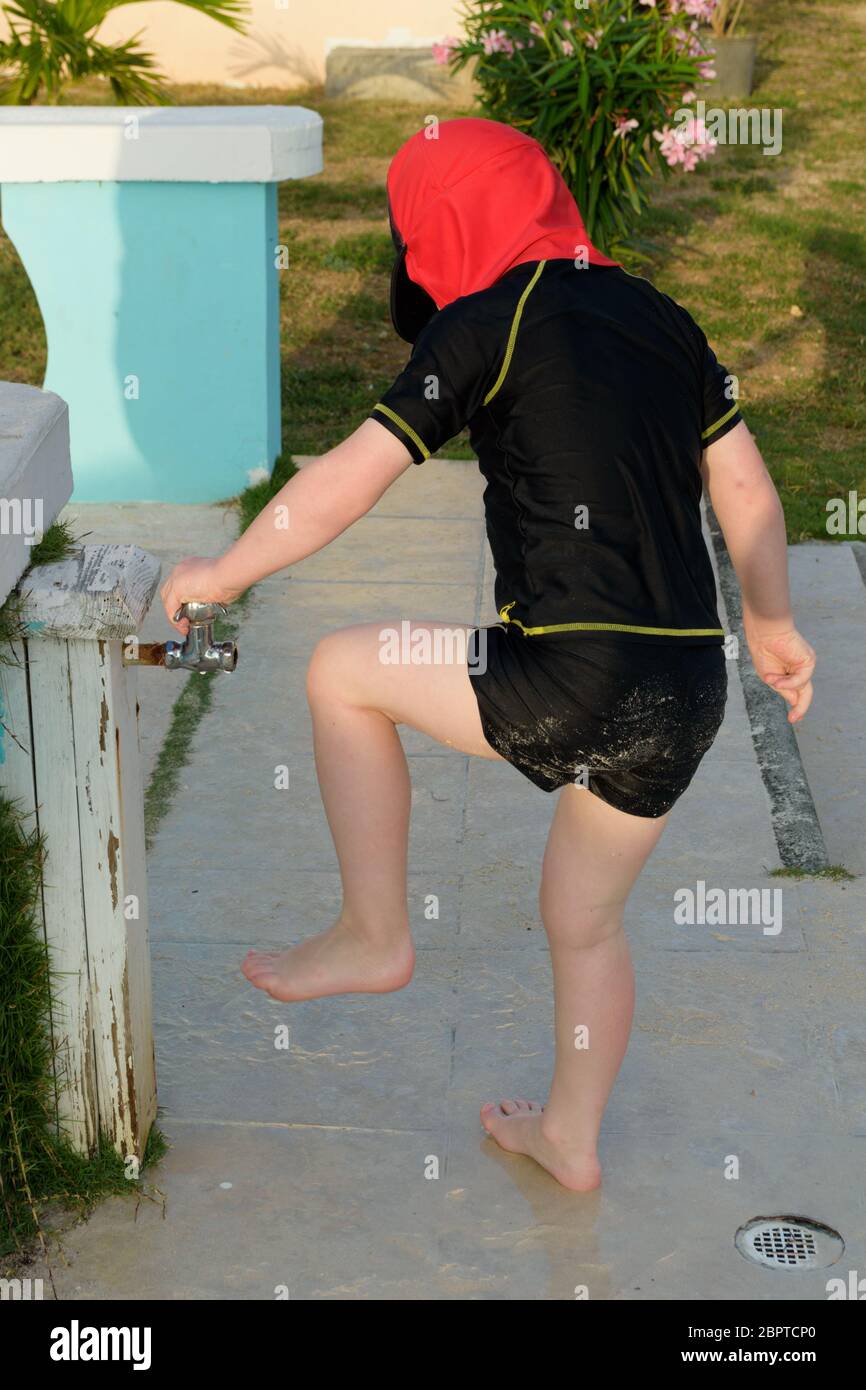 A young child about to wash the sand off their feet after playing on the beach Stock Photo