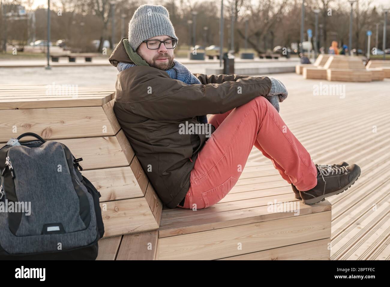 Suspicious tourist looks excitedly at his backpack and is afraid that he will be stolen while sitting on a bench in the park. Stock Photo