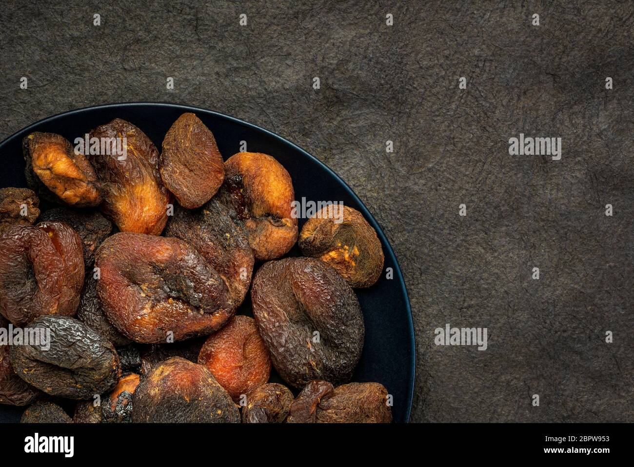 sun dried apricots - fruits on a black plate against textured bark paper with a copy spce Stock Photo