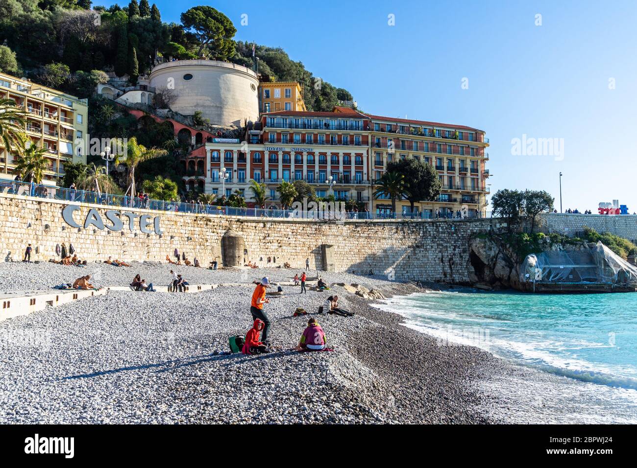 Nice, France, January 2020 - People enjoy a sunny winter day at Castel Plage in Nice with Tour Bellanda in the background Stock Photo