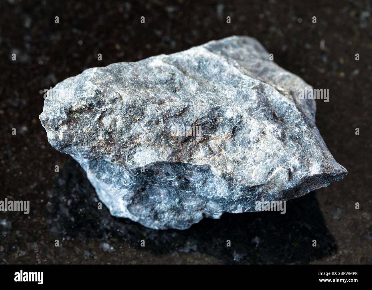 closeup of sample of natural mineral from geological collection - unpolished gray Basalt rock on black granite background Stock Photo