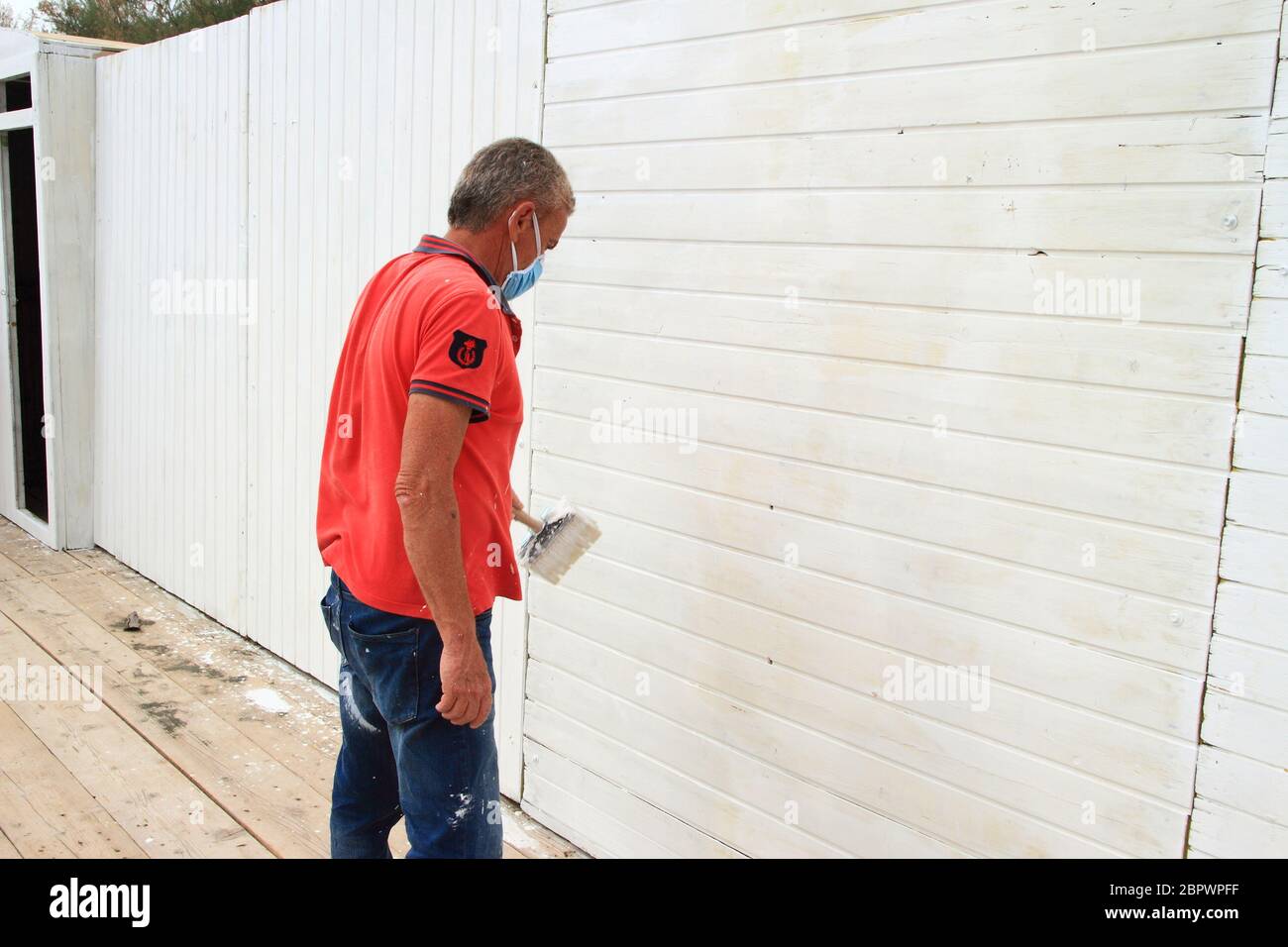 A worker paints with the white color a wall of a cabin of the lido before the reopening of the beach to customers for the new summer season. Stock Photo