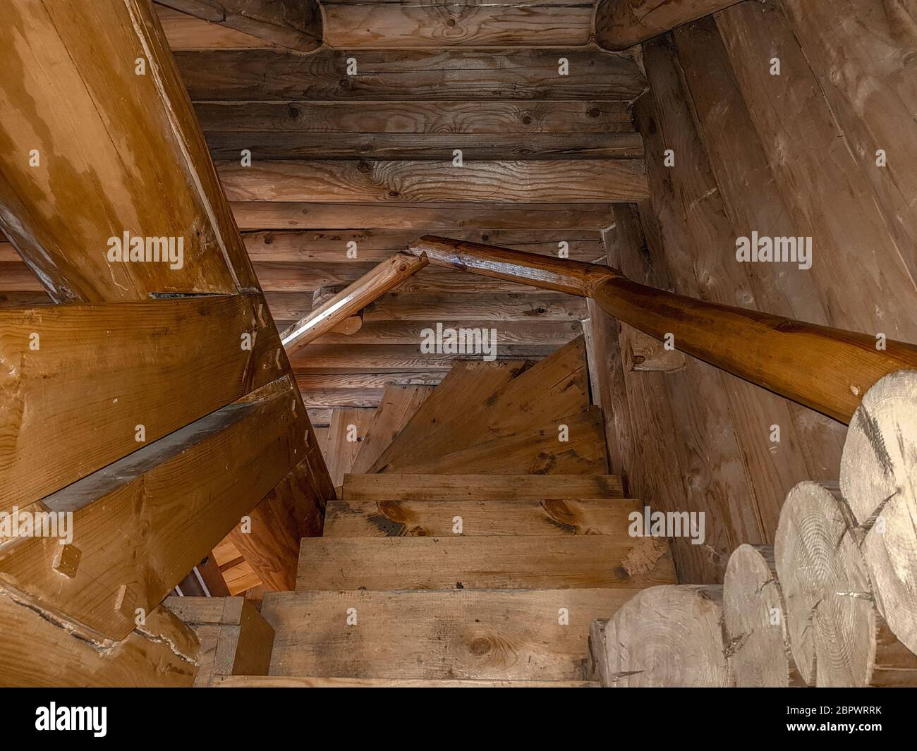 A staircase with a spiral descent, folded wooden steps, covered with a dark brown varnish of a traditional design in a house with a log house. Stock Photo