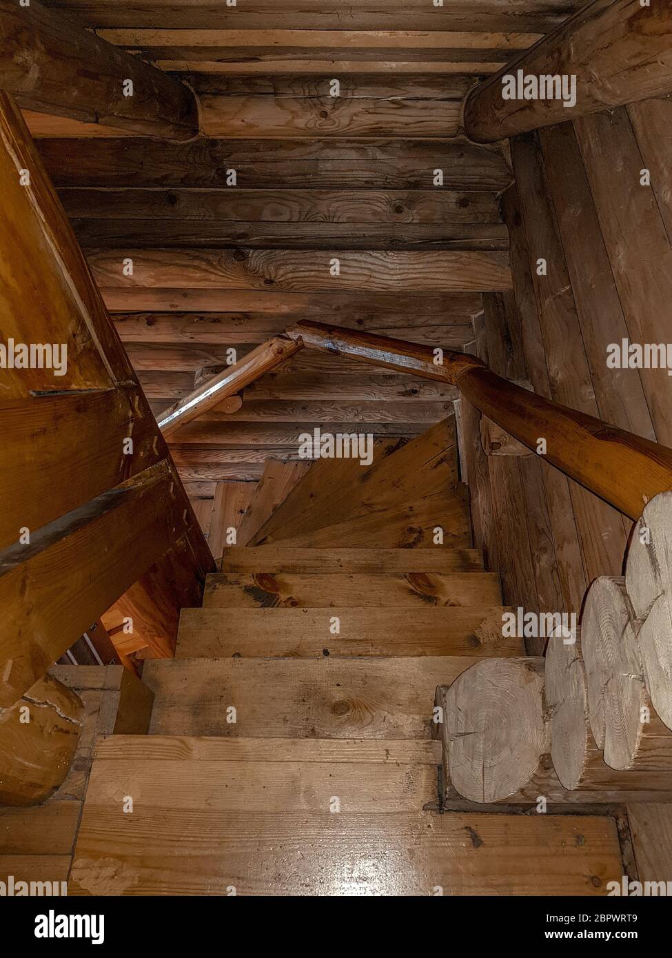 A staircase with a spiral descent, folded wooden steps, covered with a dark brown varnish of a traditional design in a house with a log house. Stock Photo