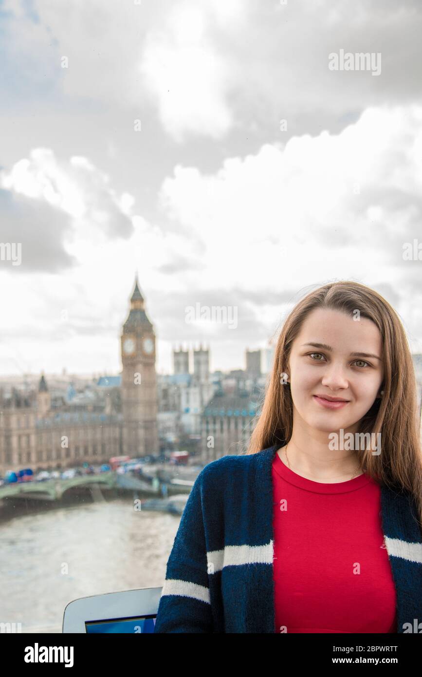 Young beautiful cute girl looks while standing in a ferris wheel cabin in London. Young pretty girl in the London Eye. Stock Photo