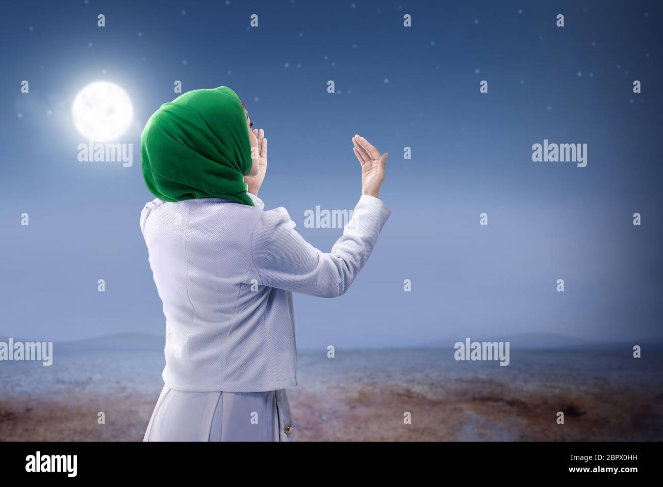 Rear view of asian muslim woman in veil raised hands and praying on the ...