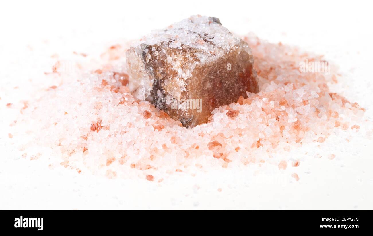rough Halite mineral in pile of grained pink Himalayan Salt on white