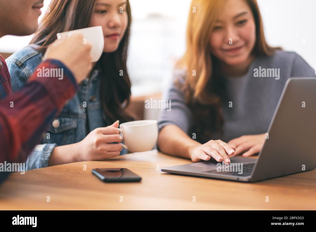 Three young asian people drinking coffee while using and looking at the same laptop computer Stock Photo