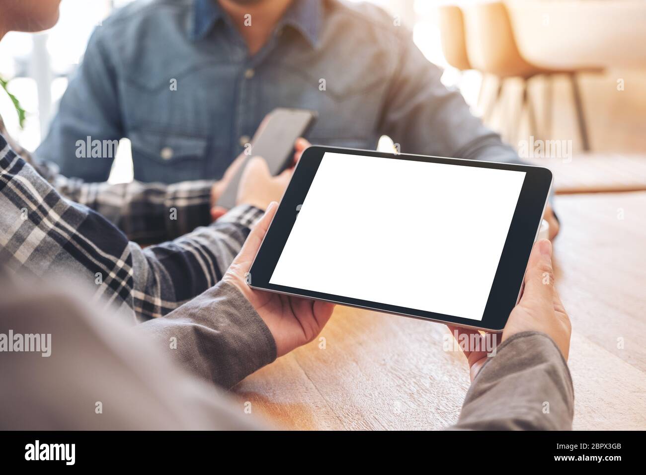 A woman using and looking at mockup tablet pc on wooden table with friends in background Stock Photo