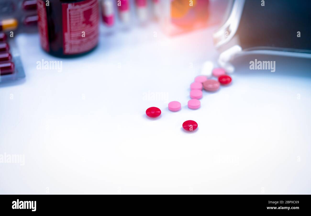 Red tablets pills on blurred background of tablets, stainless steel drug tray, and vitamin bottle. Pharmaceutical industry. Pharmacy drugstore product Stock Photo