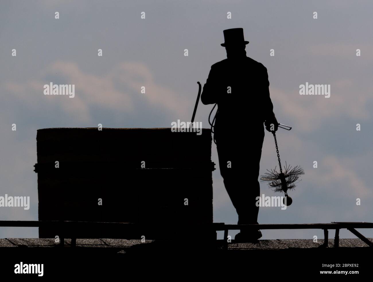 15 May 2020, Saxony, Dresden: A chimney sweep walks along a roof with his chimney sweeping tool. Photo: Robert Michael/dpa-Zentralbild/ZB Stock Photo
