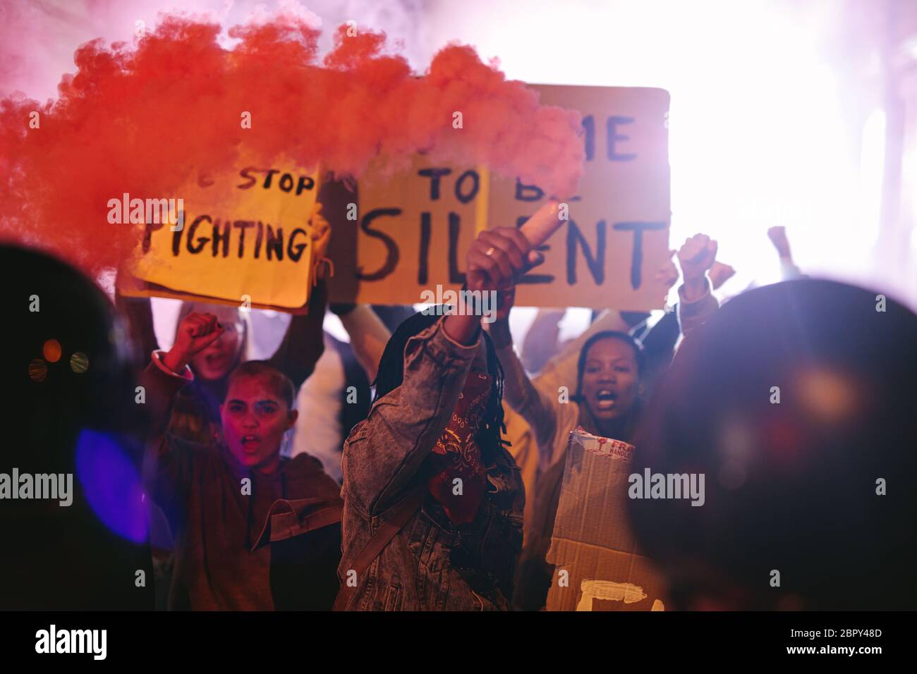 Group of people protesting with smoke grenades and banners. Group of men and women on anti-government protest at night. Stock Photo