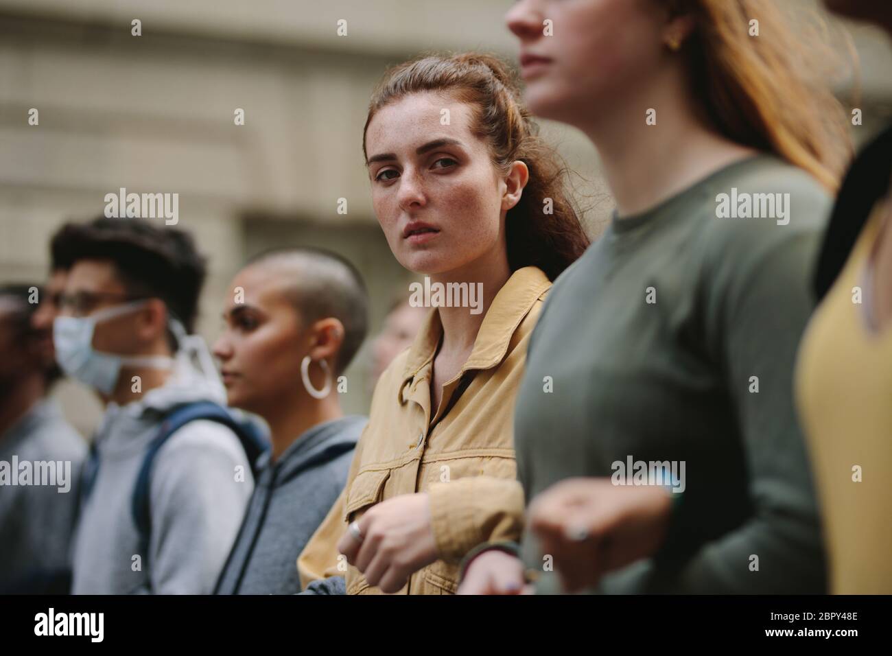 Young woman demonstrator standing in a line with people for a silent protest. Group of activists holding hands in protest picket. Stock Photo