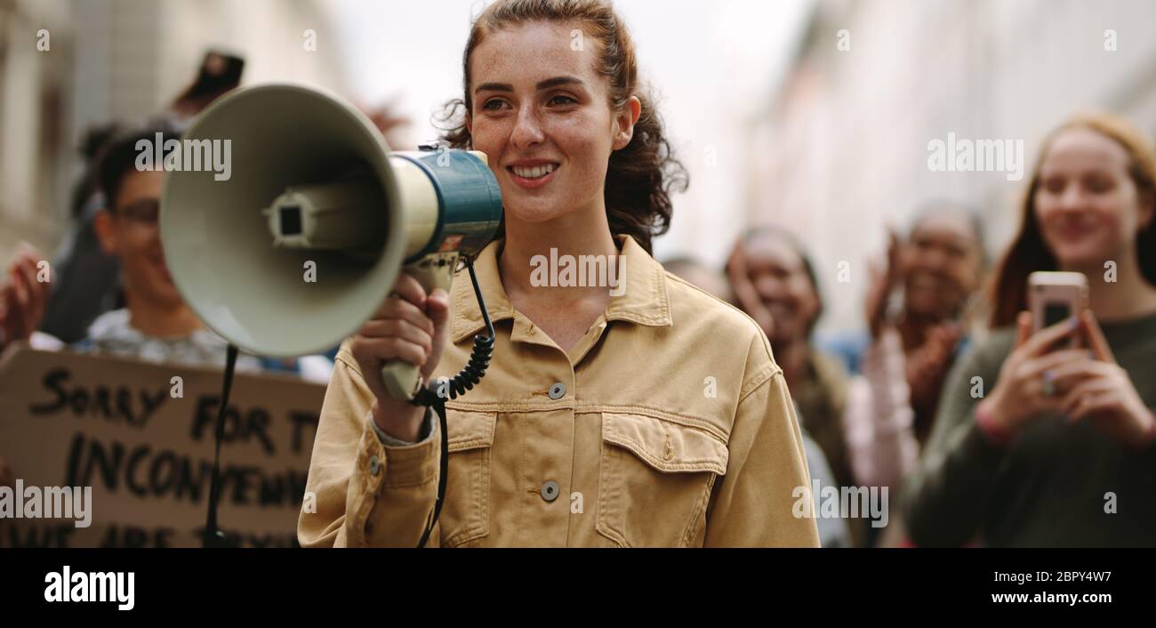 Female activist protesting at a strike, giving slogans with a megaphone. Woman demonstrator protesting with megaphone during a strike. Stock Photo