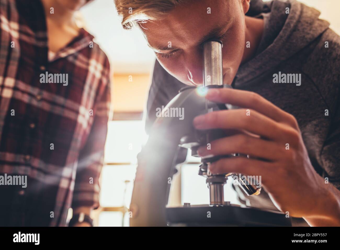 High school student using a microscope in a science class. Boy looking