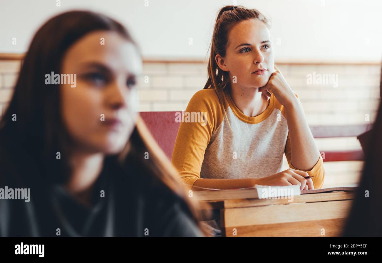 Beautiful girl sitting in class with classmates around paying attention to the lecture. Young people studying at the high school. Stock Photo
