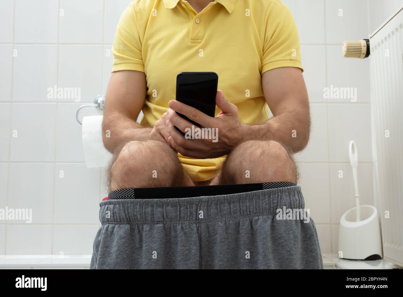 Mid-section Of Man Sitting On Toilet Using Smartphone Stock Photo