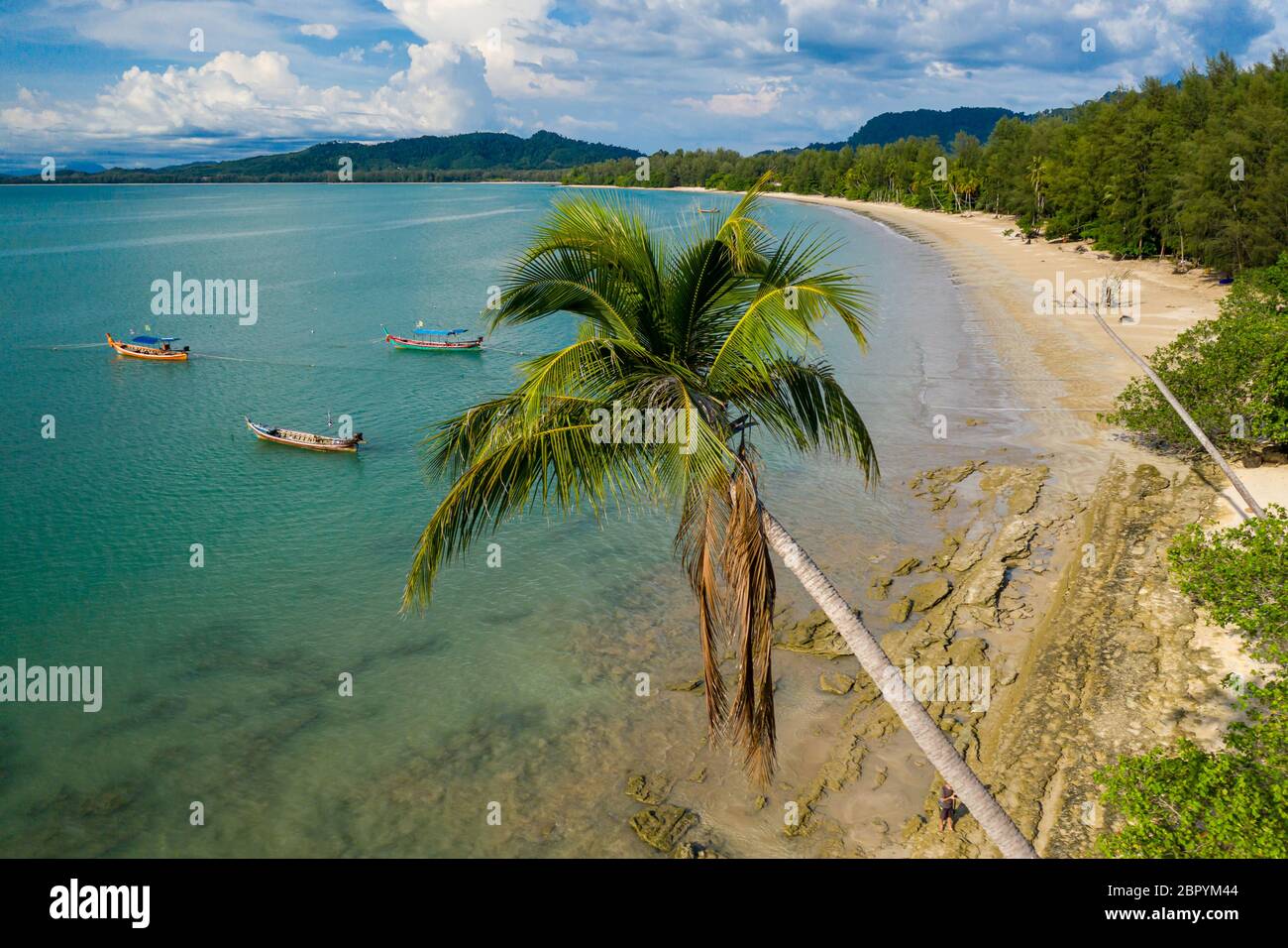 Aerial view of a beautiful, empty tropical beach surrounded by palm trees with small wooden fishing boats Stock Photo