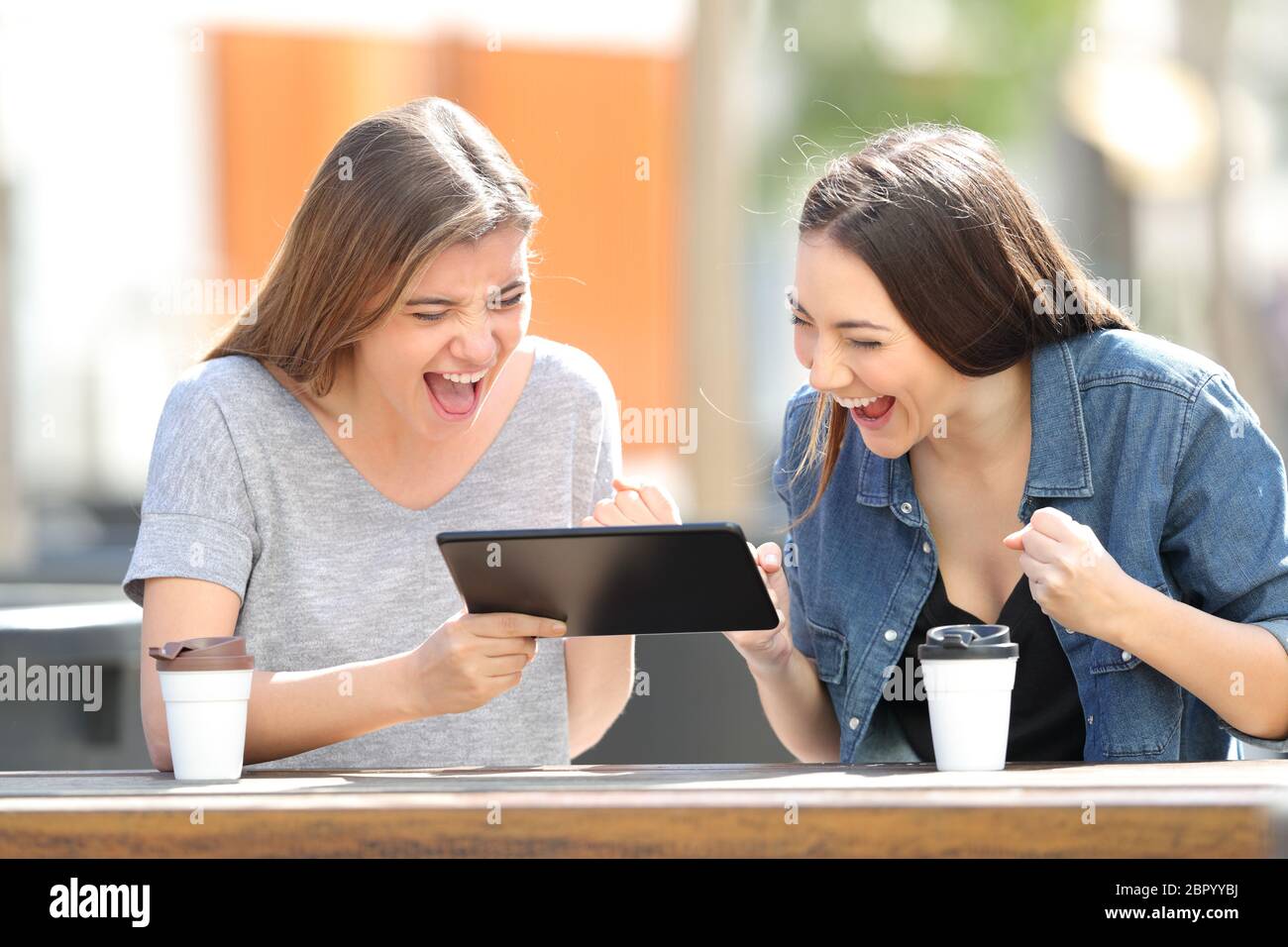 Two excited friends watching tablet online content sitting in a park Stock Photo