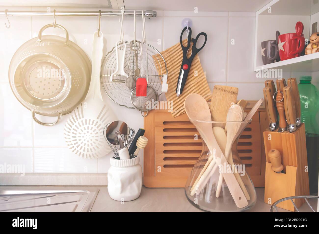 https://c8.alamy.com/comp/2BR001G/kitchen-corner-with-various-cooking-utensils-including-a-colander-knives-and-wooden-utensils-in-a-glass-container-2BR001G.jpg