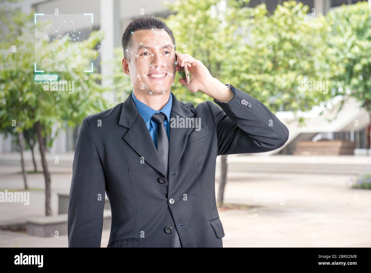 Smiling asian businessman with mobile phone using face recognition over outdoor background. Modern technology concept Stock Photo