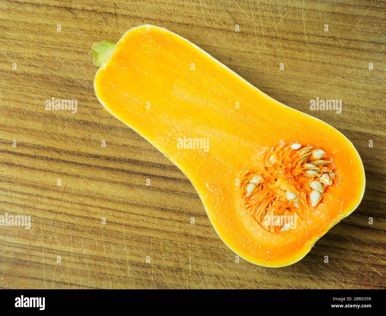 Half a butternut squash with seeds on a wooden chopping board Stock Photo