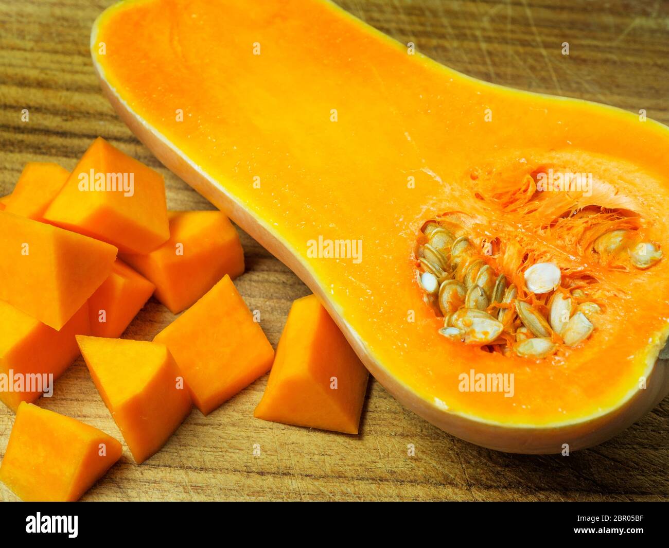 Half a butternut squash with seeds on a wooden chopping board with bit size butternut squash pieces Stock Photo