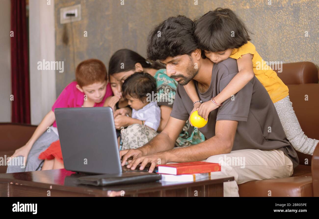 Children or kid playing by riding on father back and disturbing while father busy in working on laptop - Concept of work from home or WFH during covid Stock Photo