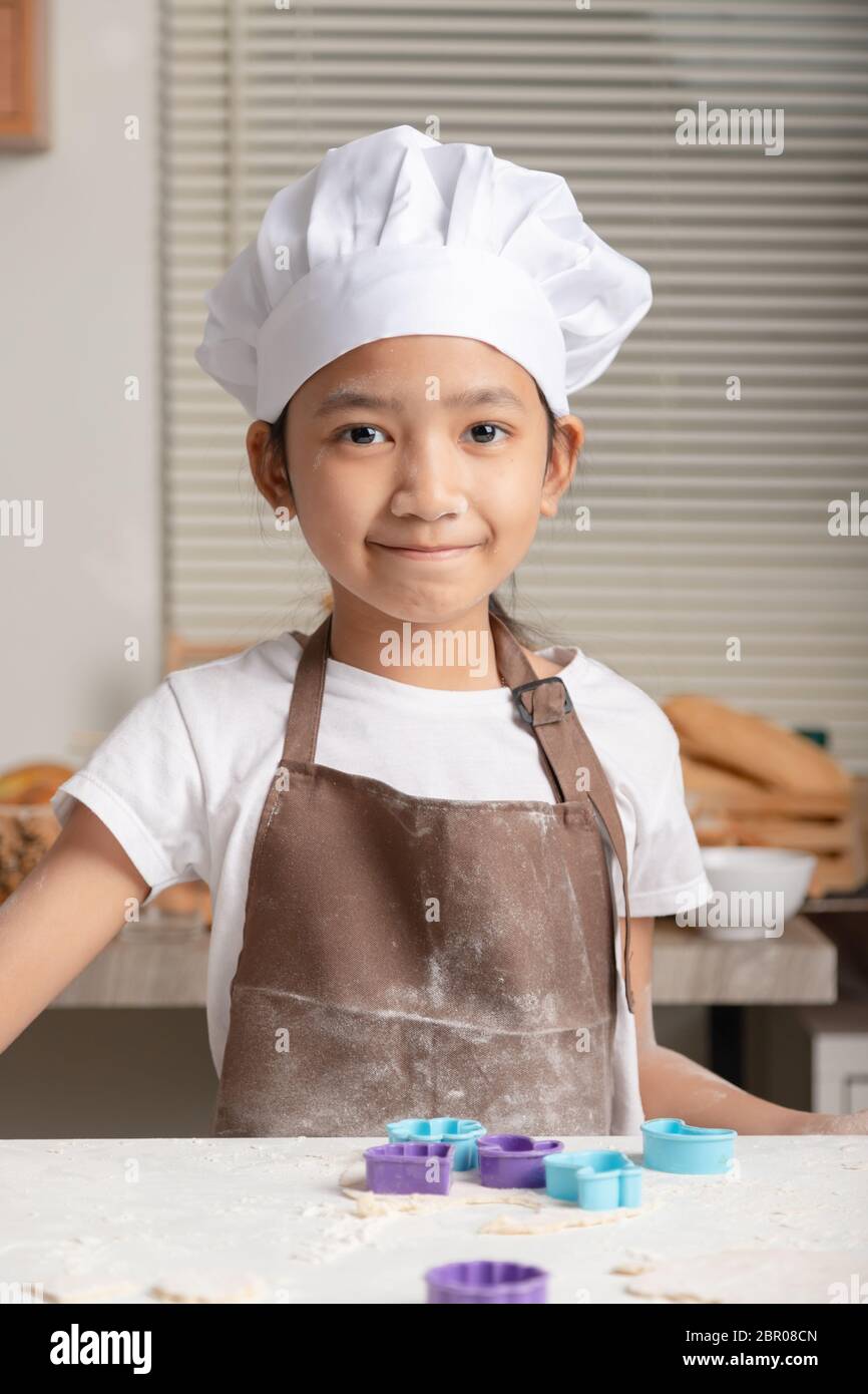 The little girl wore a white chef hat and a brown apron. The kid making