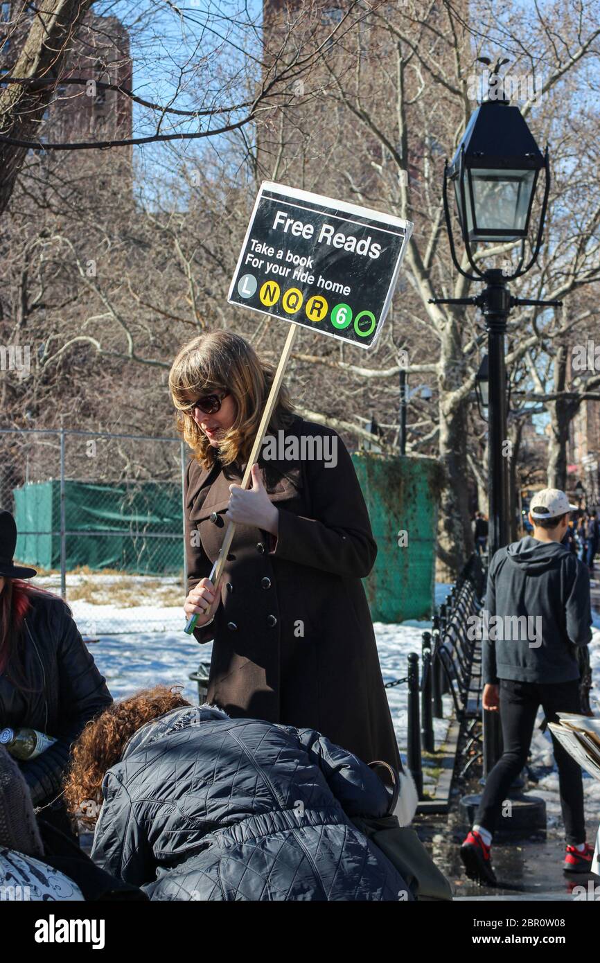 Middle-aged woman holding a Free Reads -placard and giving away used books in Washington Square Park of Manhattan, New York City, United States Stock Photo