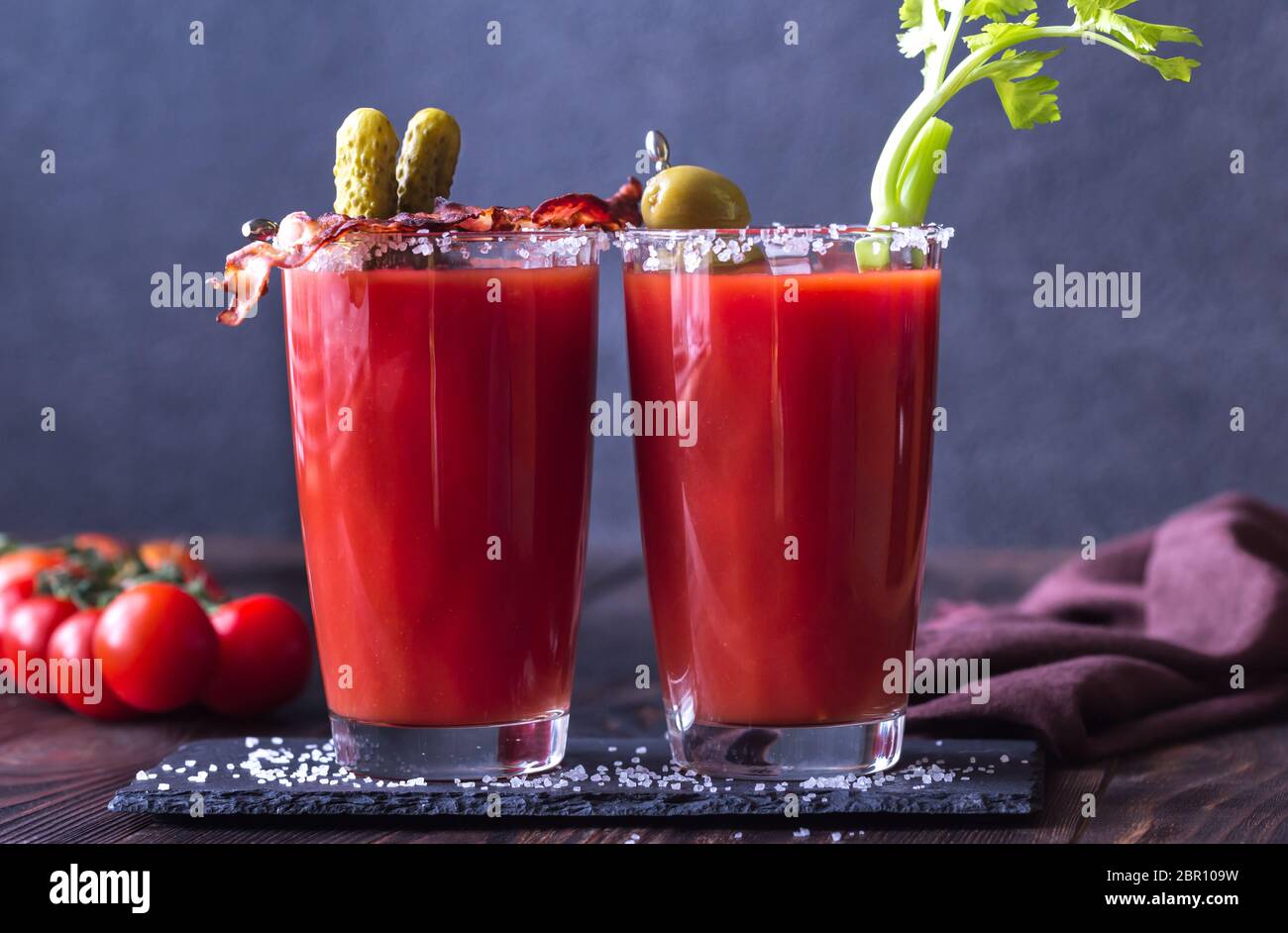 Two glasses of Bloody Mary garnished with gherkins, fried bacon strips