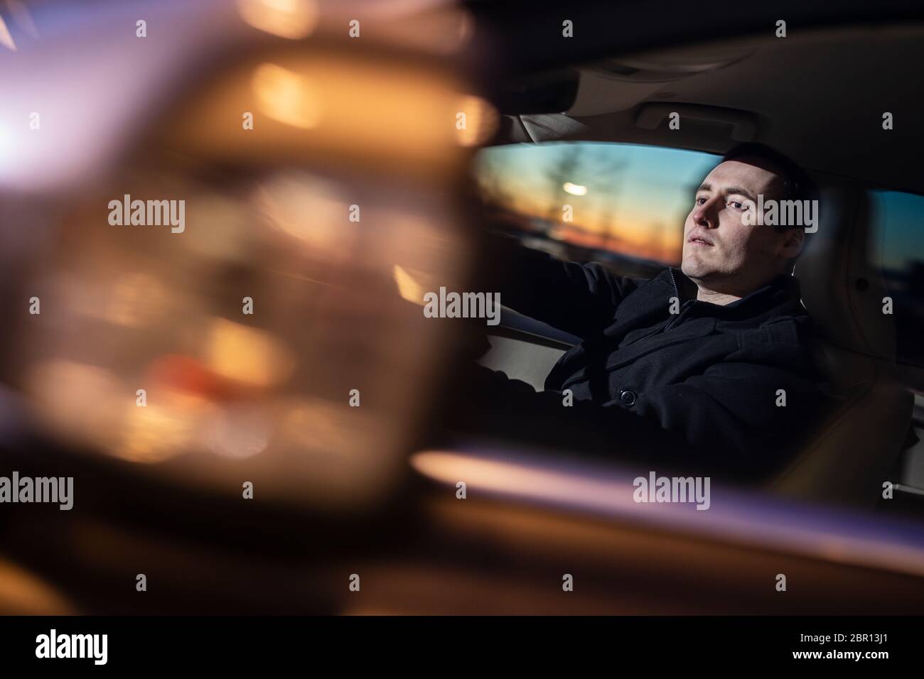 Handsome young man driving his car at night (color toned image; motion ...