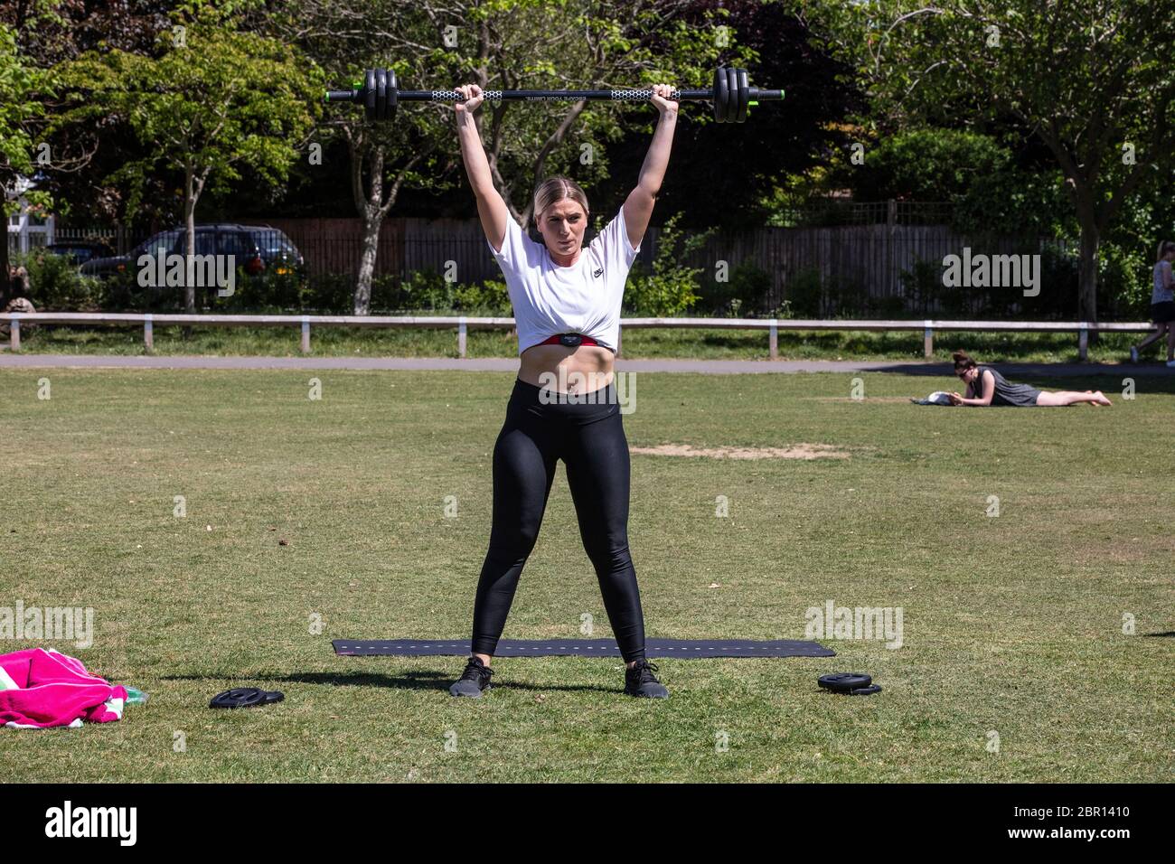 Wimbledon, London, UK. 20th May, 2020. People enjoy warmest day of 2020 during a mini heatwave this week. 20th May 2020. South Wimbledon, Southwest London, UK Chelsea Kenny from Banstead lifts wieghts whilst enjoying the warm temperature after the coronavirus lockdwon has been relaxed and people can spend more time outside in the local parks across the United Kingdom. Credit: Clickpics/Alamy Live News Stock Photo