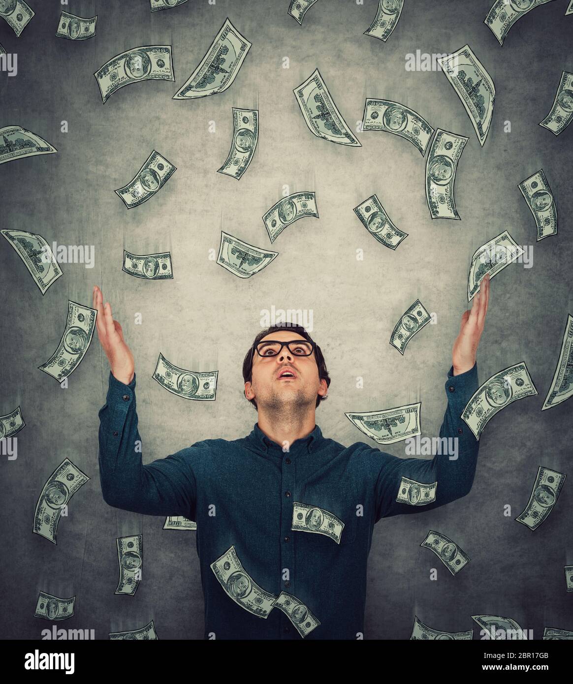 Astonished businessman raising up hands as money are falling like dollars rain. Surprised guy open mouth stunned expression, staring upwards. Lottery Stock Photo