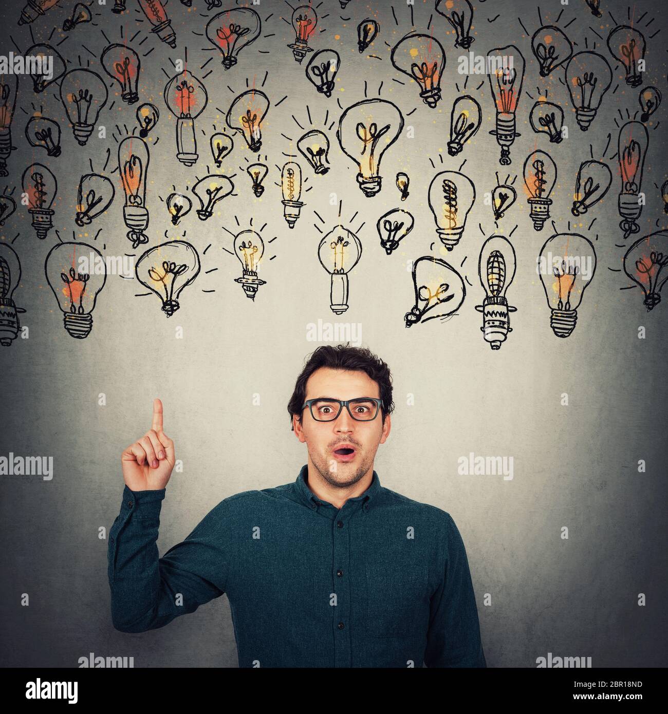 Astonished businessman, looking big eyes to camera, pointing up index finger as multiple lightbulbs float above his head. Surprised business worker, w Stock Photo