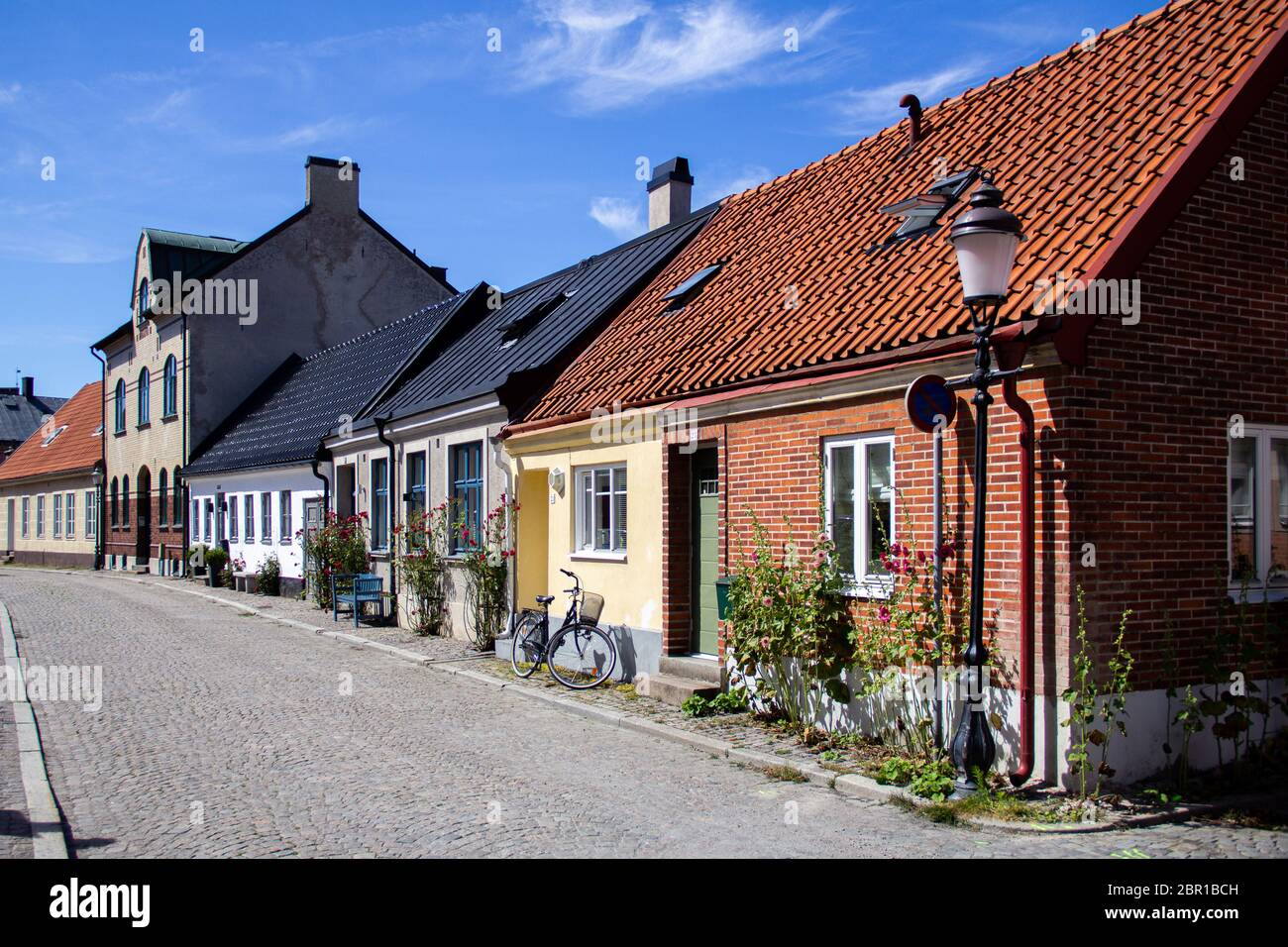 Ystad, Sweden - June 23, 2019: An empty cobblestoned street in the old town is bordered with small houses, roses and bikes Stock Photo