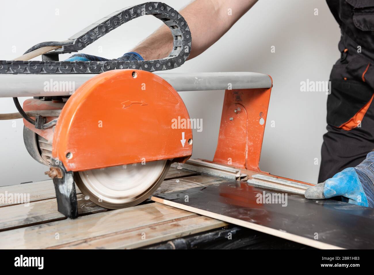 A worker is cutting a ceramic tile on a wet cutter saw machine