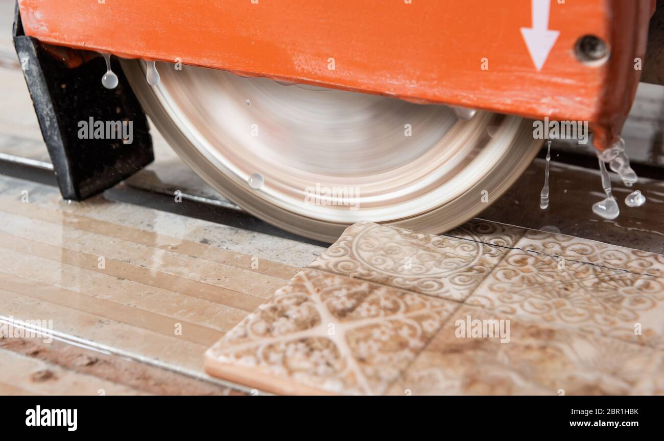 The diamond disk of a wet saw cuts through a ceramic tile Stock Photo