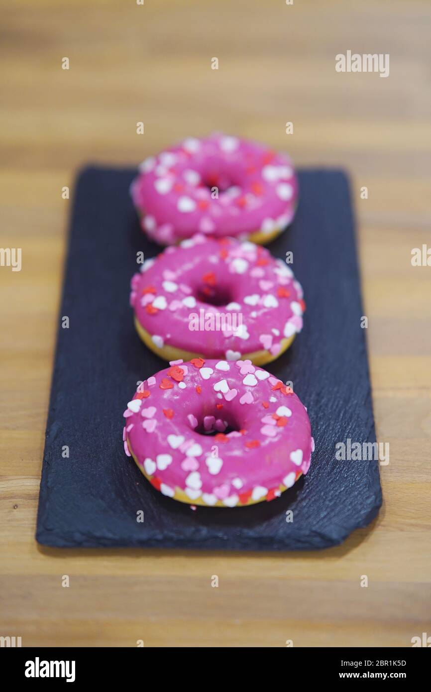Three Pink donuts on a black tray. Stock Photo