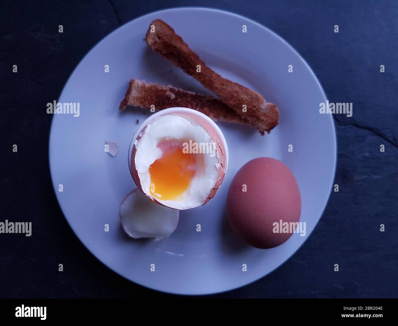 Two boiled breakfast eggs, one cut open in an egg cup, wuth strips of